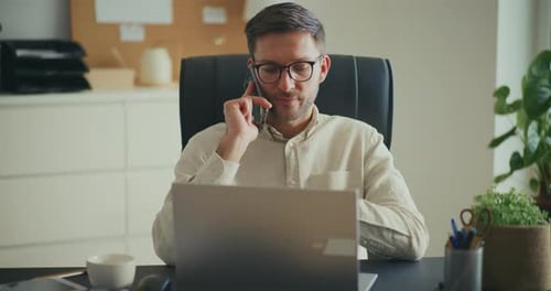 Man Using Laptop and Talking on Phone in Office