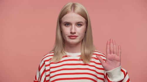 Ernsthafte Frau macht Stop-Geste mit erhobener Hand auf rosafarbenem Hintergrund