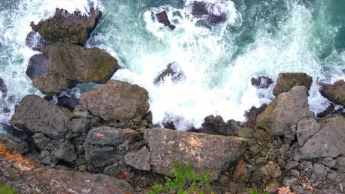 Eine Drohnenaufnahme einer großen Meereswelle trifft auf die großen Felsen am Strand. Das Plätschern der krachenden Welle