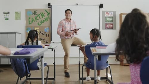 Biracial male teacher teaching diverse students in classroom at elementary school