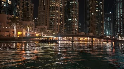 Passengers Traveling By Boat On A River With A View Of The Cityscape At Night