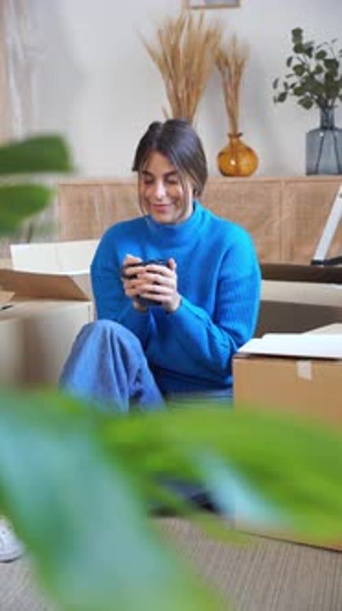 Woman Relaxing With Phone Surrounded by Moving Boxes