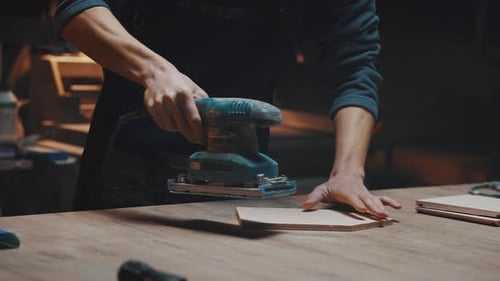 Close Up of a Carpenters Hands with a Grinder A Young Apprentice Guy Works in a Carpentry Workshop