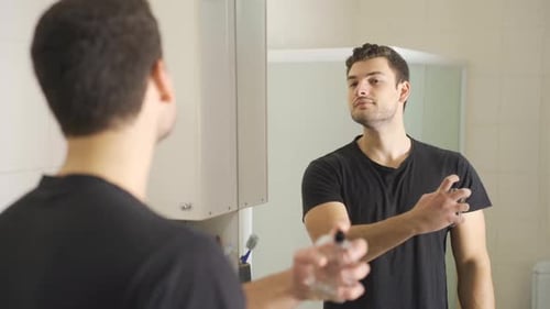 Handsome Man Sprays Cologne in Bright Bathroom Mirror