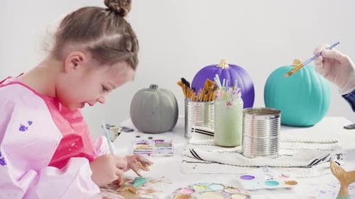 Child Paints Mermaid with Pumpkins on Table
