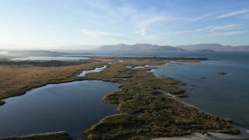 Aerial view of serene wetlands and mountains at sunset near a tranquil lake.