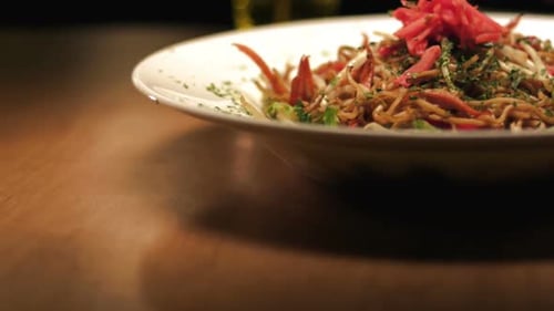 Close up shot of bowl of yakisoba noodles with a drink in the background