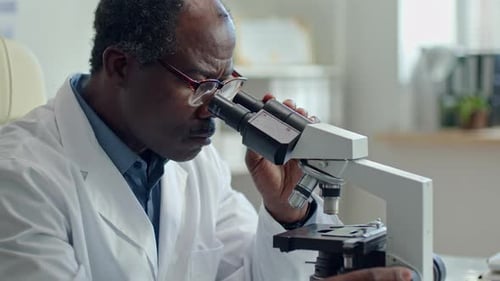 Reifer schwarzer Wissenschaftler benutzt Mikroskop während der Forschung