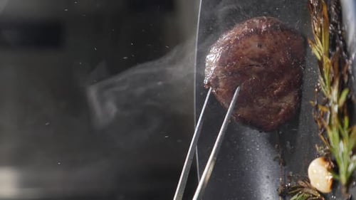 Steak sizzling in pan with rosemary and garlic