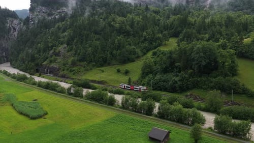 Luftaufnahme eines Zuges, der durch ein üppiges grünes Tal in den Schweizer Alpen fährt