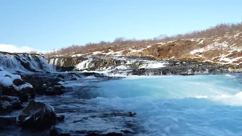 Gros plan de la cascade de Brúarfoss avec de l'eau bleue et des berges enneigées en Islande