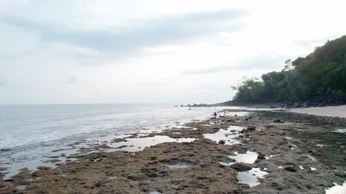 Woman on rocky tropical beach looking at the ocean