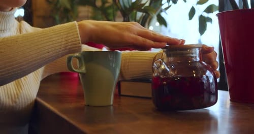 Woman Pours Red Tea into Mug in Cafe