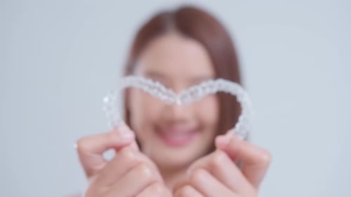Smiling Young Woman Holding Clear Aligners in Heart Shape