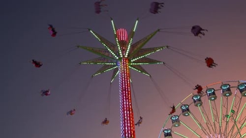 Illuminated sky flyer festival ride, swinging up high in the sky against sunset dusk sky.