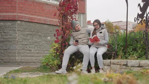 Lovers Seated Outdoors As Man Warmly Pulls Woman Close While She Reads in Breeze