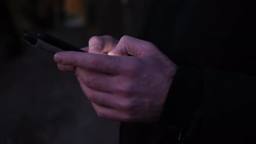 Closeup of man's hands typing on the smartphone in the night. Side view in 4k