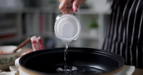 Asian woman is pouring water into an electric pot