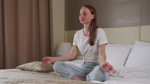 Young Woman Meditating on Bed in Peaceful Bedroom