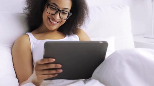 Smiling Woman Using Tablet in White Bed