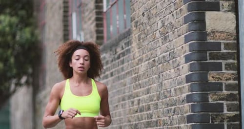 Young adult female checking activity tracker on a run in urban city