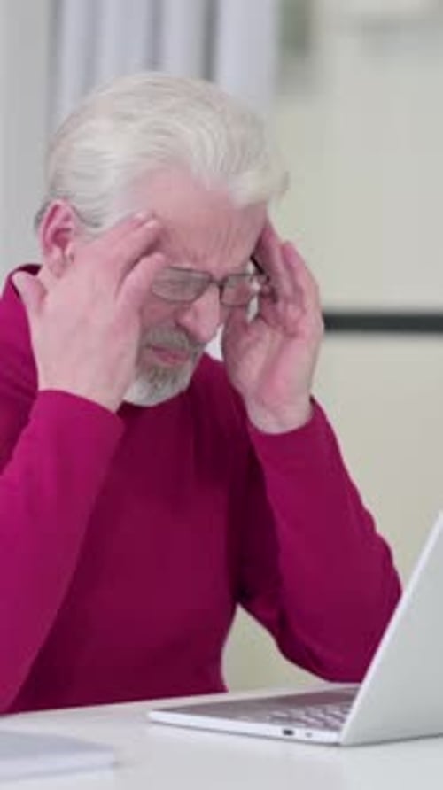 Senior Man Using Laptop Massaging Eyes Due to Strain