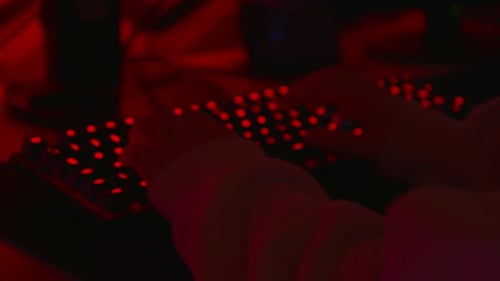Anonymous hacker in a dark red room typing on red keyboard.