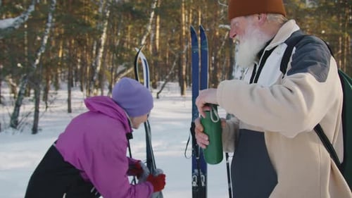 Cheerful Elderly Skiers Enjoying Hot Tea and Resting in Winter Forest