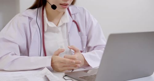 Closeup asian female doctor sitting at desk using laptop during telemedicine consultation, hand