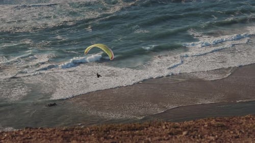 Aerial view of a paraglider flying above the ocean waves near the coastline