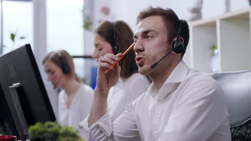 Nahaufnahme: Junger Mann, seriöser Servicemitarbeiter, spricht mit Kundenanrufen im geschäftigen Callcenter-Büro