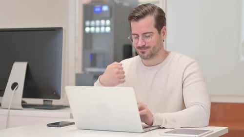 Man Working on Laptop, Rubbing Wrist in Office