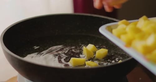 Hand Adds Diced Potatoes To Frying Pan