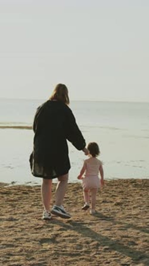 A Person and a Child Leisurely Walking Together Along the Beach During a Stunning Sunset Vertical
