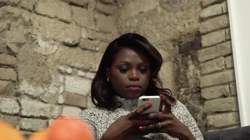 Mujer negra estadounidense con teléfono móvil en un sofá, foto casual a mano.