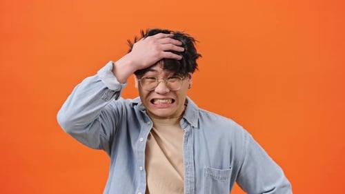Confused Asian Man Puts Hands on Head with Scared Expression