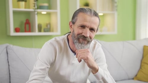 Mature man sitting on sofa in living room at home and smiling.