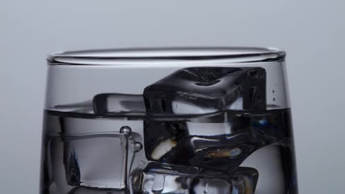 Close Up Of Ice Cubes Falling In A Glass Of Drinking Water On The Light White Screen Background