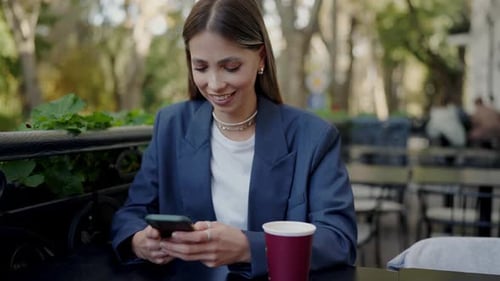 Stylish Pretty Woman Sitting at Cafe Table and Chatting Online Using Smartphone