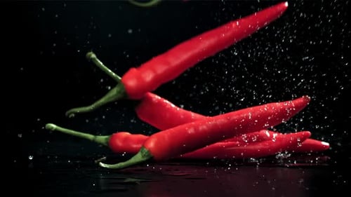 Chili Peppers fallen auf einen nassen schwarzen Tisch, gefilmt mit einer Hochgeschwindigkeitskamera mit 1000 Bildern pro Sekunde