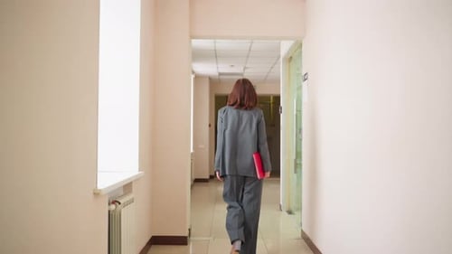 Businesswoman Walking in Office Hallway Holding Red Folder with Purpose