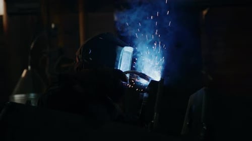 Schweißer mit Schutzmaske arbeitet mit Lötlampe in einer Industriefabrik