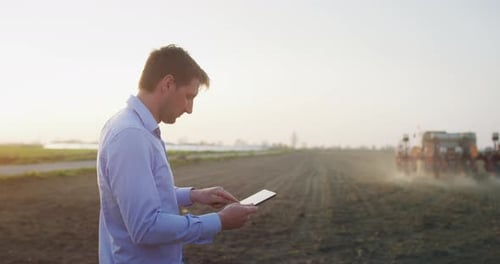 Farmer Using Tablet Supervising Tractor in Rural Field