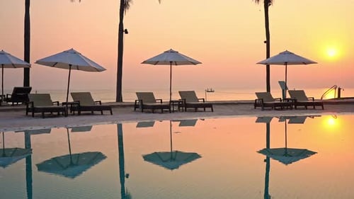Summertime: Beautiful view of the sunset at the hotel pool area. Line of Beach deck chairs and umbre