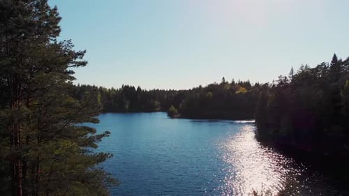 Cinematic ascending aerial shot of deep blue lake surrounded by wilderness, lush coniferous forest.