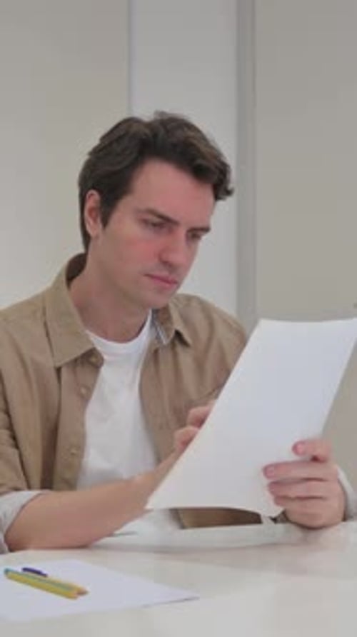 Man Reviewing and Comparing Documents at Desk