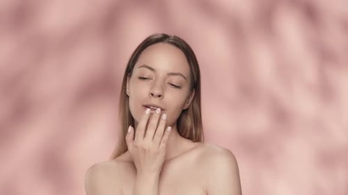 A Charming Woman Touches Her Lips While Moisturizing Them in the Studio on a Pink Background Close