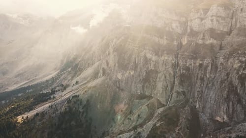 Distant aerial view of a high mountain waterfall with misty sunflares in Tzoumerka, Greece