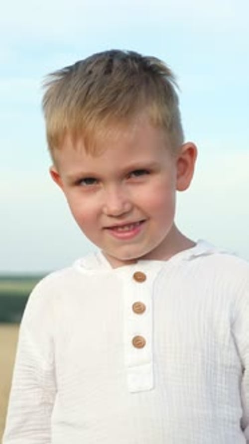 Chemise en lin blanc décontractée pour garçon blond souriant debout dans un champ, douce et dorée
