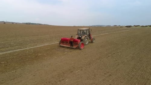 Tractor, agricultural machinery and workers sow a field - aerial tracking shot